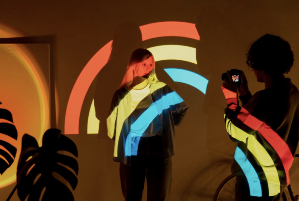 Mujeres proyectadas con luces de arcoíris en un ambiente artístico, reflejando diversidad, empoderamiento y cultura pop contemporánea.